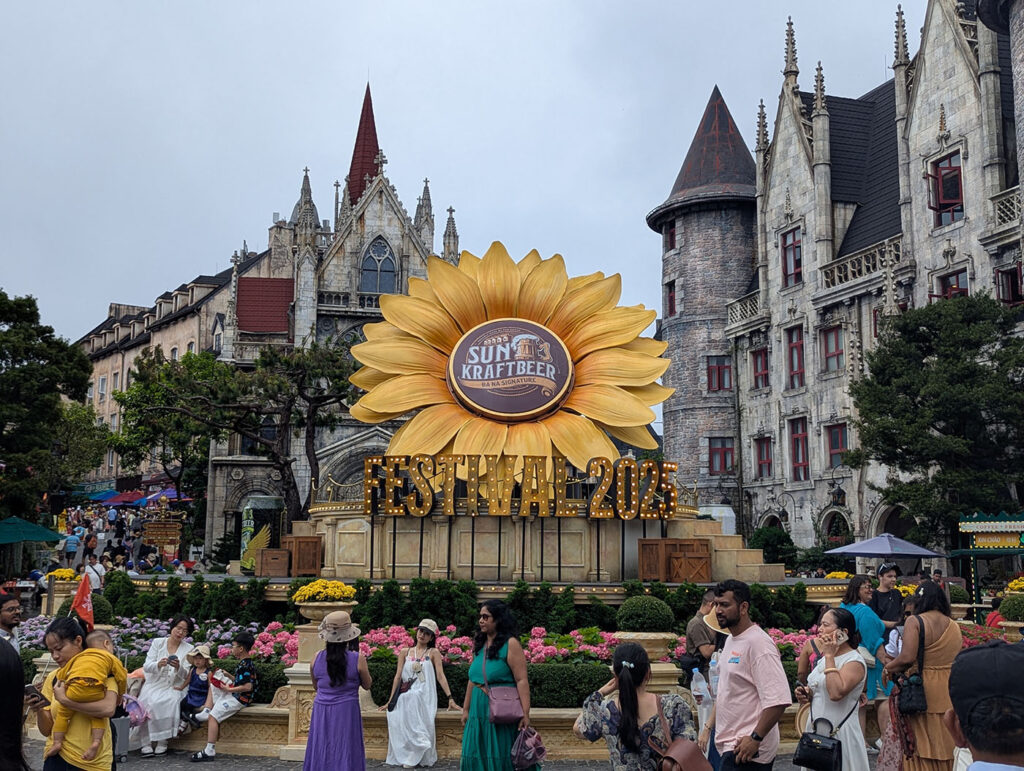 ヨーロッパ風の建物を背景に、大きなひまわりのオブジェが中央に設置されている。「SUN KRAFT BEER FESTIVAL 2025」と書かれており、多くの観光客が記念撮影を楽しんでいる。